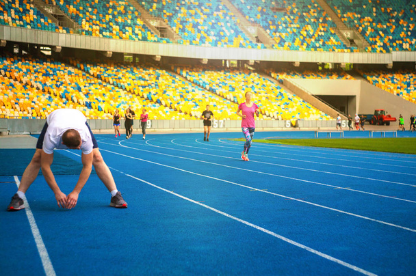 Группа спортсменов делает упражнения на стадионе. Спортсмены отдыхают после тренировки
. - Фото, изображение