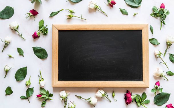 Verspreide rose bloemen rond zwarte schoolbord met copyspaceon licht marmeren achtergrond platte lay Top View - Foto, afbeelding