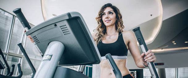 Attractive muscular smiling fitness woman running on treadmill i - Photo, Image