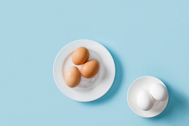 top view of fresh brown and white eggs on white plates on blue background - Foto, Imagem