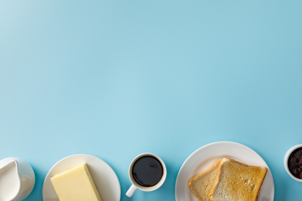 top view of milk, butter, jam, cup of coffee and two toasts on white plates on blue background - Fotografie, Obrázek