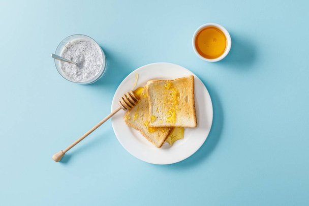 top view of yogurt with chia seeds, toasts with honey and honey dipper on white plate on blue background - Foto, imagen