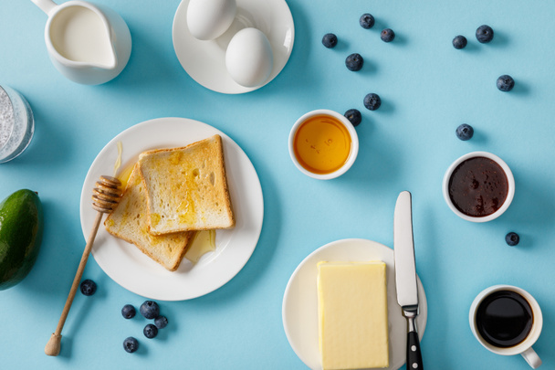 vista superior del desayuno servido con aguacate y arándanos dispersos sobre fondo azul
 - Foto, Imagen