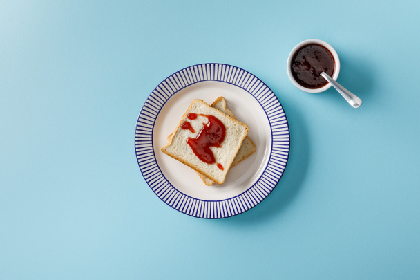 top view of toasts on plate and spoon in bowl with jam on blue background - Photo, Image