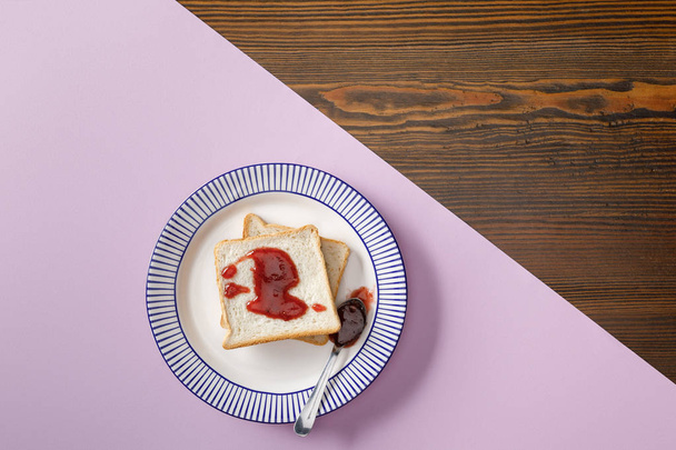 top view of toasts, spoon with jam on violet and wooden background - Photo, Image