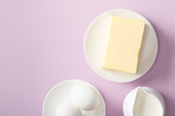 vista superior de mantequilla, leche y huevos cocidos en platos blancos sobre fondo violeta
 - Foto, Imagen