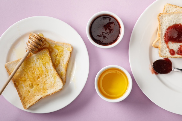 top view of toasts with jam and honey, bowls and wooden dipper on violet background - Foto, afbeelding
