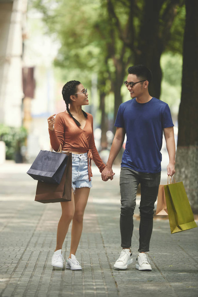 Happy Asian para z torby na zakupy trzymając ręce i chodzenie wzdłuż ulicy w mieście - Zdjęcie, obraz