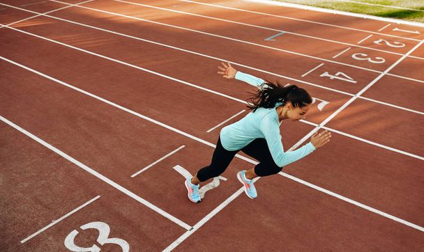Outdoor horizontal image of young woman athlete running on racetrack at stadium. View from above of sportswoman during running training session for competition. People, sport and healthy lifestyle - Fotoğraf, Görsel
