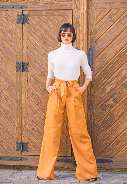Girl with makeup posing in fashionable clothes. Fashionable outfit slim tall lady. Fashion and style concept. Woman walk in loose pants. Woman fashionable brunette stand outdoors wooden background - Photo, Image