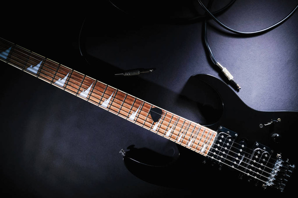 Modern black electric guitar with jack cable on black background - Foto, afbeelding