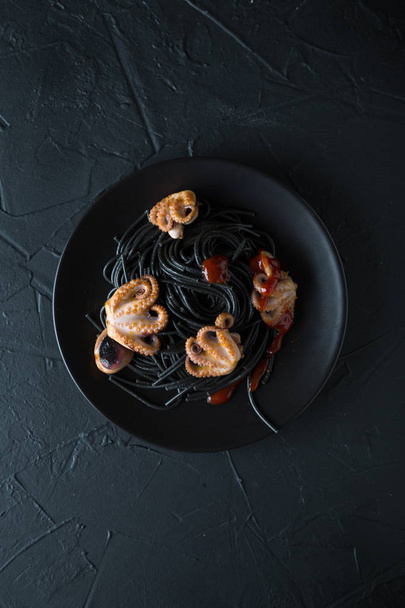 Black pasta with octopus on black background - Foto, immagini