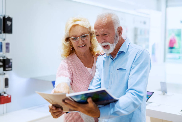Carino sorridente caucasico coppia anziana guardando il catalogo nel negozio di tecnologia
. - Foto, immagini