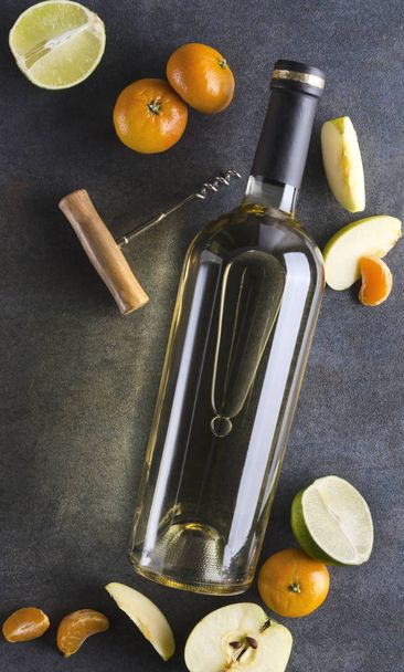 Vertical shot.Bottle of white wine, corkscrew and fresh fruits on the grey surface, top view - Photo, Image