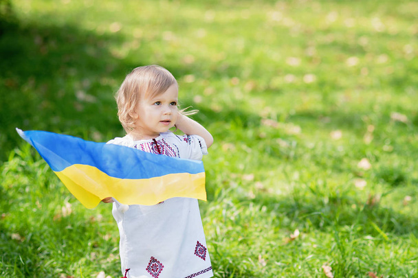 Lapsi kantaa lepattava sininen ja keltainen lippu Ukrainan alalla. Ukrainan itsenäisyyspäivä. Lippupäivä. Perustuslakipäivä. Tyttö perinteisessä kirjonta lipun Ukrainan. - Valokuva, kuva