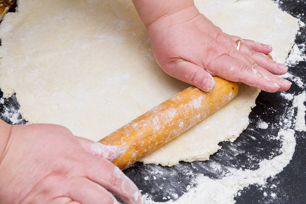 Rolling out the raw dough with a wooden rolling pin on the table - Photo, image