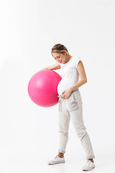 Beautiful young pregnant yoga fitness woman posing isolated over white wall background make exercises with ball. - Fotó, kép
