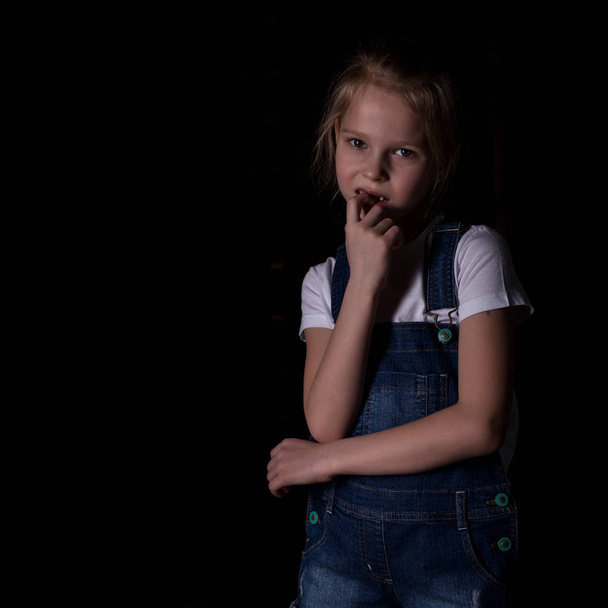 beautiful blonde little girl on a dark background. She stands in different poses and shows different emotions. free space for your text - Фото, изображение