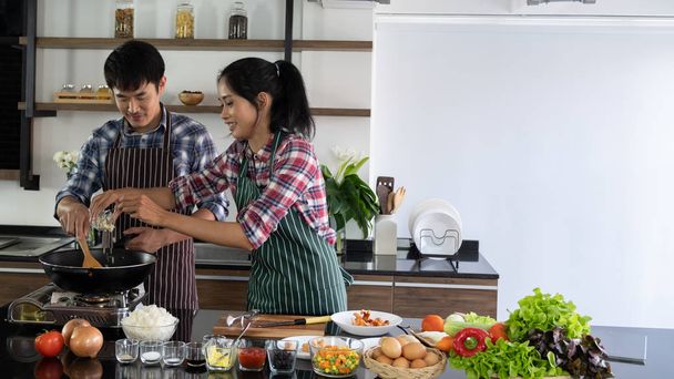 Молодая азиатская пара с удовольствием готовит вместе, две семьи помогают друг другу готовиться на кухне
. - Фото, изображение