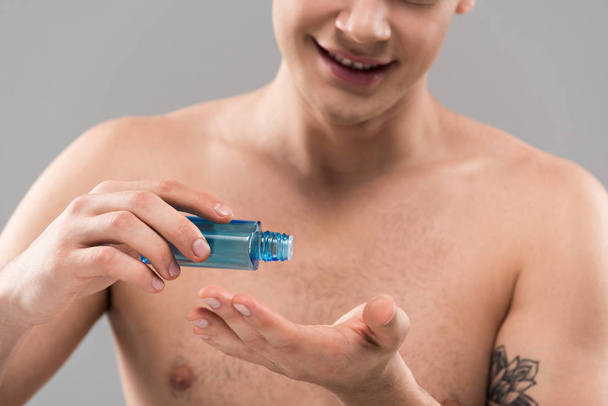 cropped view of smiling naked young man applying lotion on hand isolated on grey - Zdjęcie, obraz