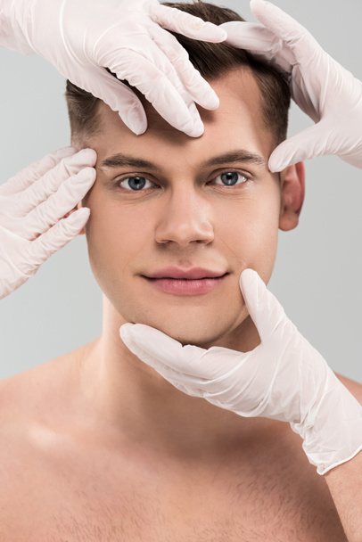 partial view of cosmetologists in latex gloves touching face isolated on grey - Fotoğraf, Görsel