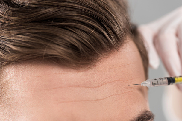 Teilansicht des Kosmetikers bei Schönheitsinjektionen in die Stirn isoliert auf grau - Foto, Bild