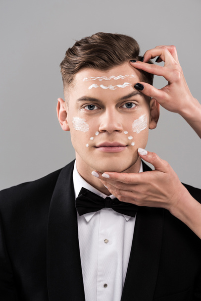 partial view of cosmetologists applying cream and man in formal wear isolated on grey - Foto, Bild