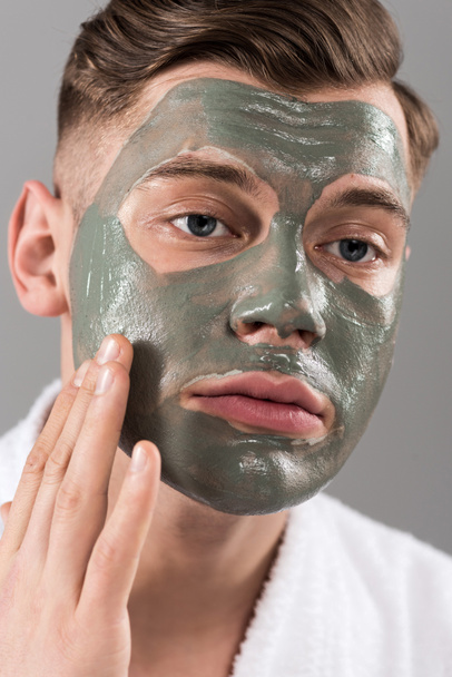 sad young man touching clay mask isolated on grey - Foto, immagini