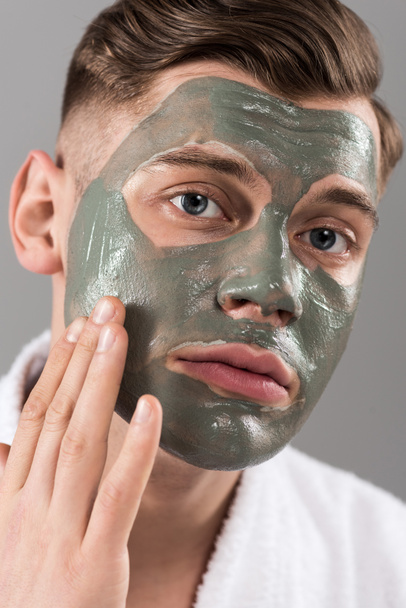 sad young man touching clay mask isolated on grey - Zdjęcie, obraz
