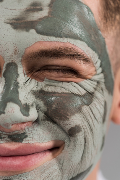 cropped view of smiling young man with clay mask with closed eye - Foto, afbeelding