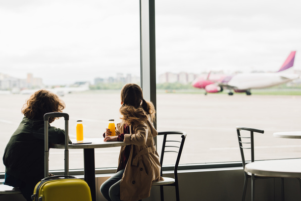 iki çocuk bekleyen salonda oturan ve uçakta pencere bakıyor - Fotoğraf, Görsel