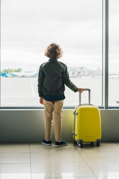 takana näkymä poika seisoo lähellä ikkunaa, jolla keltainen matkalaukku
 - Valokuva, kuva