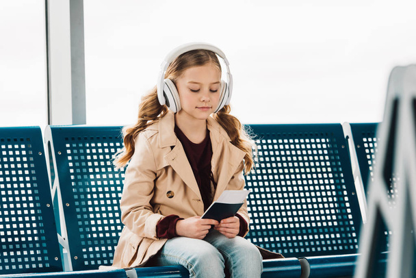 enfant préadolescent assis sur un siège bleu, tenant un passeport et écoutant de la musique dans la salle d'attente à l'aéroport
  - Photo, image