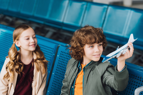 cute preteen kids sitting in waiting hall and playing with toy plane - Foto, immagini