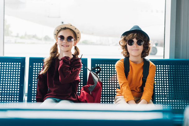 cute preteen kids in sunglasses sitting in waiting hall - Foto, afbeelding