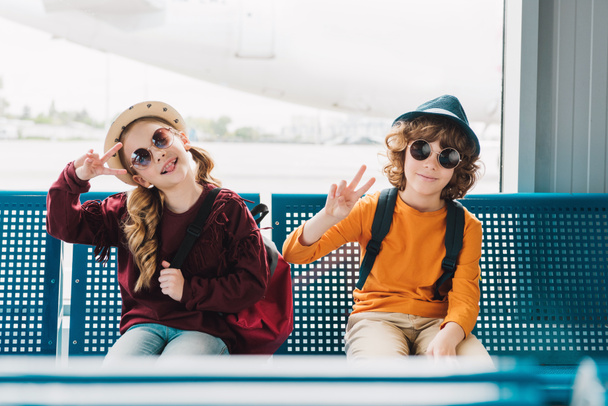 preteen kids in sunglasses sitting in waiting hall and showing peace signs - Φωτογραφία, εικόνα