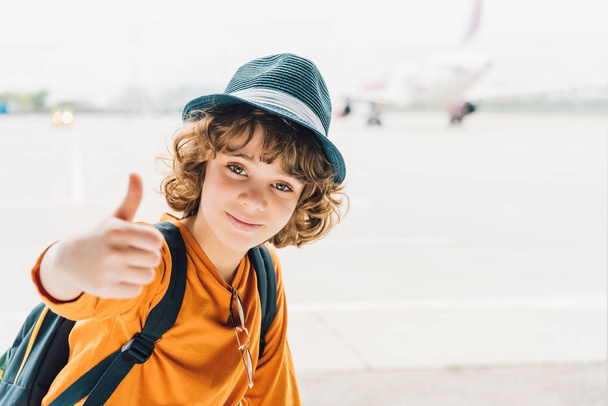 ανήλικου αγόρι κοιτάζοντας την κάμερα και δείχνοντας αντίχειρας στο αεροδρόμιο - Φωτογραφία, εικόνα