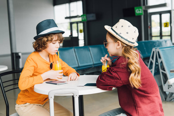 preteen kids sitting at table with orange juice in departure lounge - 写真・画像