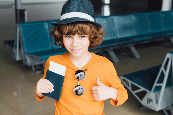 Netter Junge mit Pass und Flugticket zeigt Daumen nach oben am Flughafen - Foto, Bild