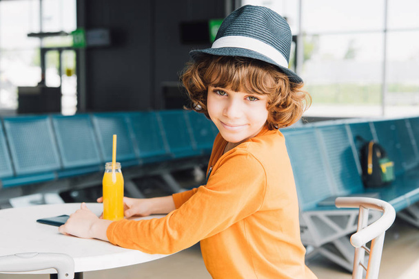 słodkie preteen chłopiec siedzi przy stole z sokiem pomarańczowym w poczekalni - Zdjęcie, obraz