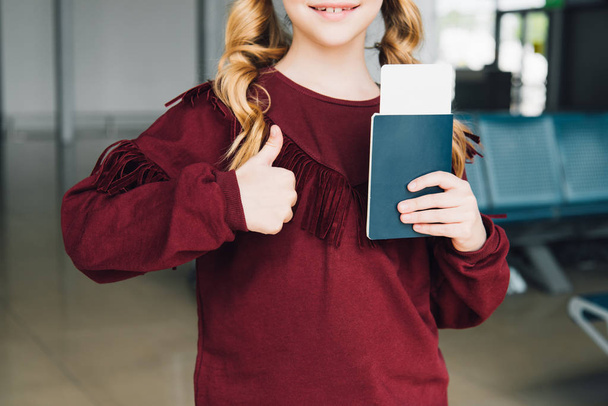 обрезанный вид подростка с паспортом и авиабилетом, показывающим большой палец вверх в аэропорту
 - Фото, изображение