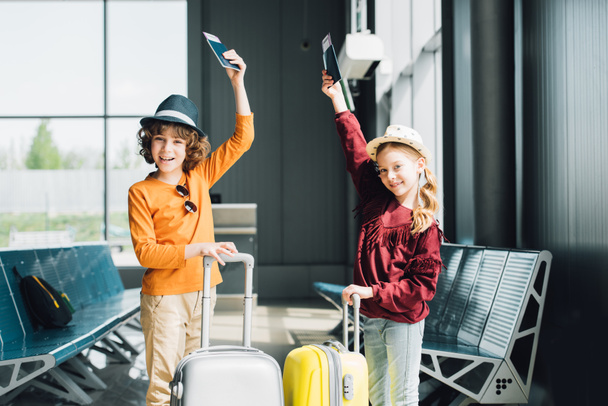 ευτυχισμένο Προεφηβικό παιδιά με βαλίτσες, αεροπορικά εισιτήρια και διαβατήρια στην αίθουσα αναμονής - Φωτογραφία, εικόνα