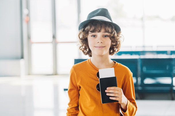 niño preadolescente con pasaporte y billete de avión en el aeropuerto mirando a la cámara
 - Foto, Imagen
