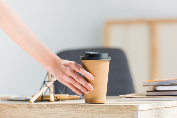 cropped view of woman holding coffee to go near stationary and notebooks  - Photo, Image