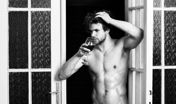 Beginning great evening. Man with sexy torso drink wine. Sexy attractive macho tousled hair coming out through bedroom door. Bachelor sexy body. Sexy lover concept. Guy smooth skin posing seductive - Photo, Image