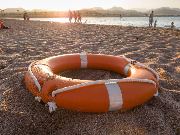 Image rapprochée de l'anneau de sauvetage en plastique rouge sur une plage de sable fin au coucher du soleil
 - Photo, image
