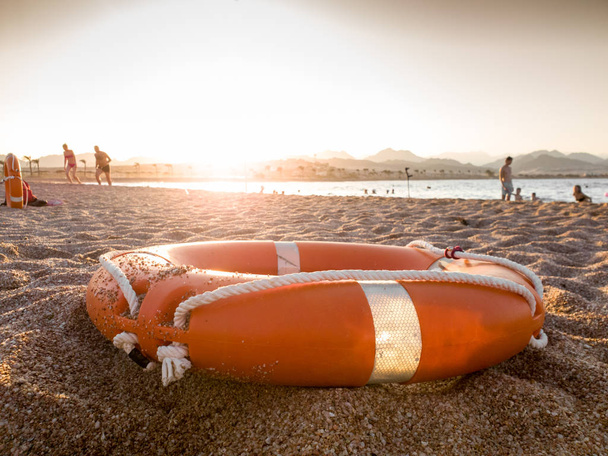 Image rapprochée de l'anneau de sauvetage en plastique rouge sur une plage de sable fin au coucher du soleil
 - Photo, image