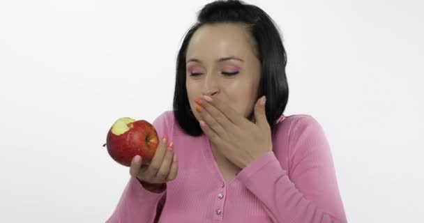 Young beautiful woman eating big, fresh and juicy red apple on white background - Кадры, видео
