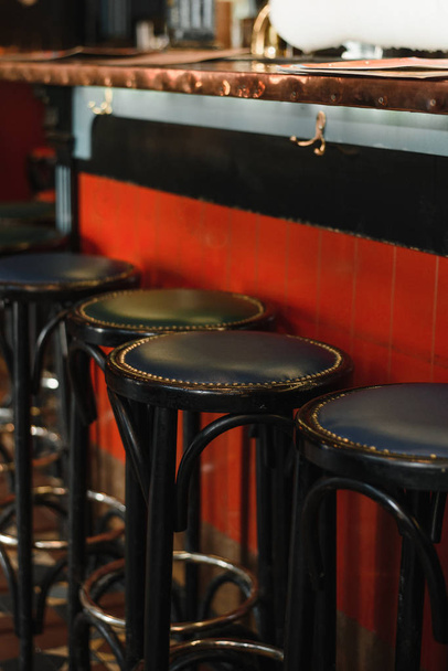 Row of wooden leather stools inside a vintage style bar. Side view of bar counter - Photo, Image