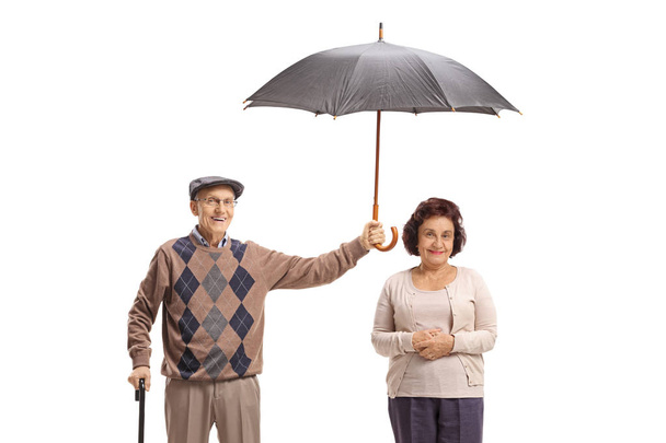 Elderly gentleman holding an umbrella over an elderly lady - Fotoğraf, Görsel